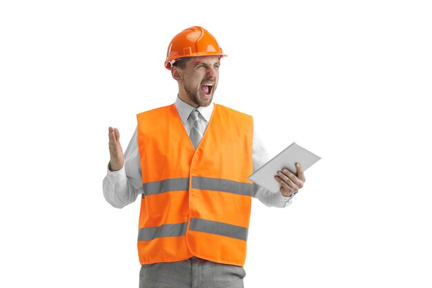 The builder in a construction vest and an orange helmet with tablet. Safety specialist, engineer, industry, architecture, manager, occupation, businessman, job concept