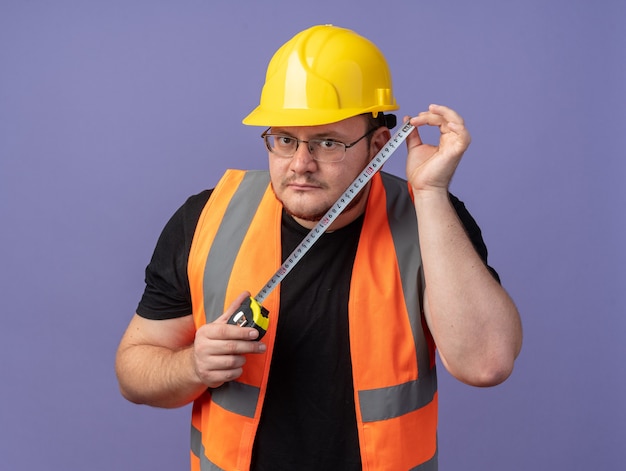 Free photo builder man in construction vest and safety helmet holding measure tape looking at camera surprised