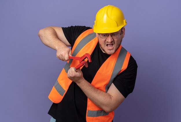 Builder man in construction vest and safety helmet holding wrench looking emotional and worried