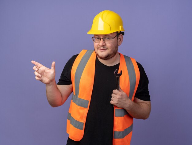 Builder man in construction vest and safety helmet looking at camera pointing