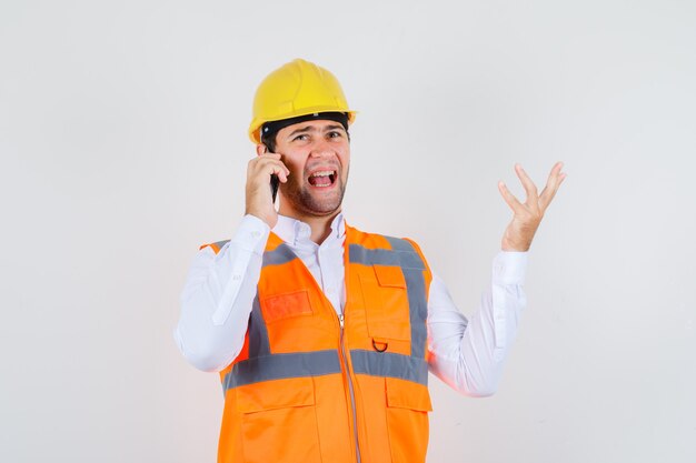 Строитель человек злится во время разговора по смартфону в рубашке, униформе, вид спереди.