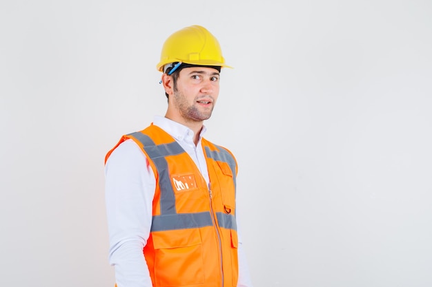 Builder man standing with pencil behind his ear in shirt, uniform and looking positive , front view.