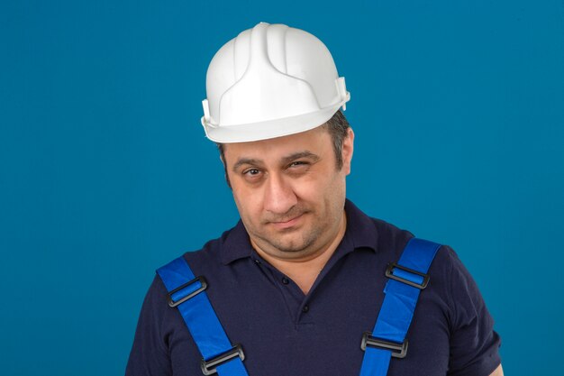 Человек-строитель в строительной форме и защитном шлеме с подозрением смотрит на синюю стену