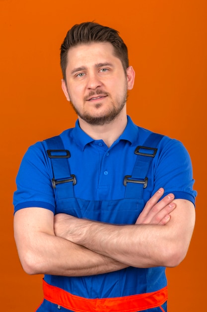 Free photo builder man wearing construction uniform standing with arms crossed with confident smile over isolated orange wall
