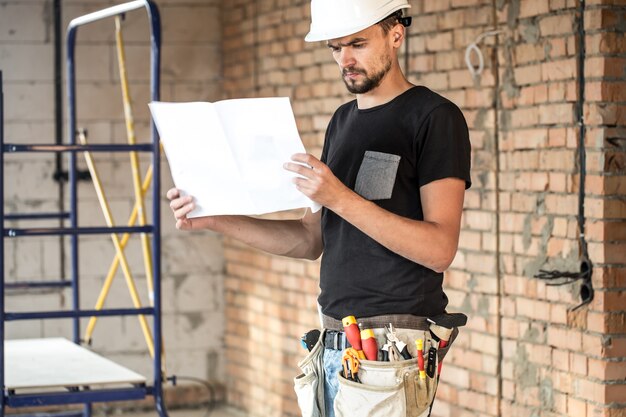 Builder with construction tools at construction site, looking blueprint