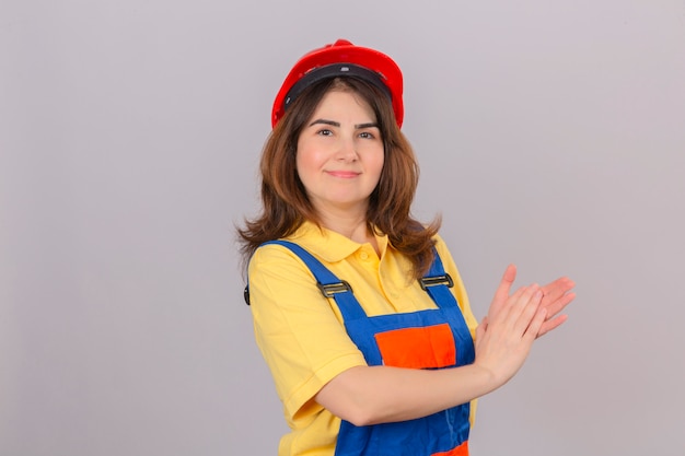 Builder woman wearing construction uniform and safety helmet applauding after presentation smiling over isolated white wall