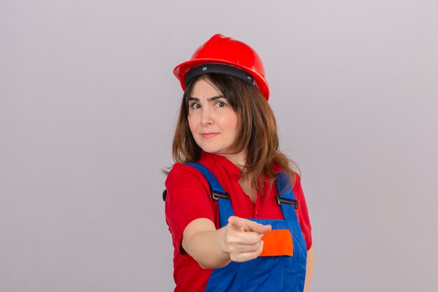 Женщина-строитель в строительной форме и защитном шлеме недовольно и разочарованно смотрит в камеру над изолированной стеной