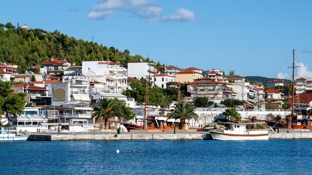 複数の緑のある丘の上にある建物、前景に係留されたボートのある桟橋、ネオスマルマラス、ギリシャ