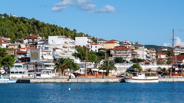 複数の緑のある丘の上にある建物、前景に係留されたボートのある桟橋、ネオスマルマラス、ギリシャ