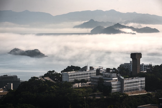 Buildings surrounded by trees, water and mountains covered in fog