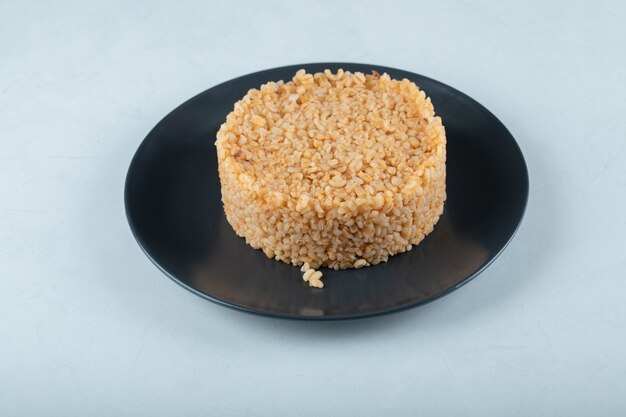 Bulgur rice on dark plate on white.