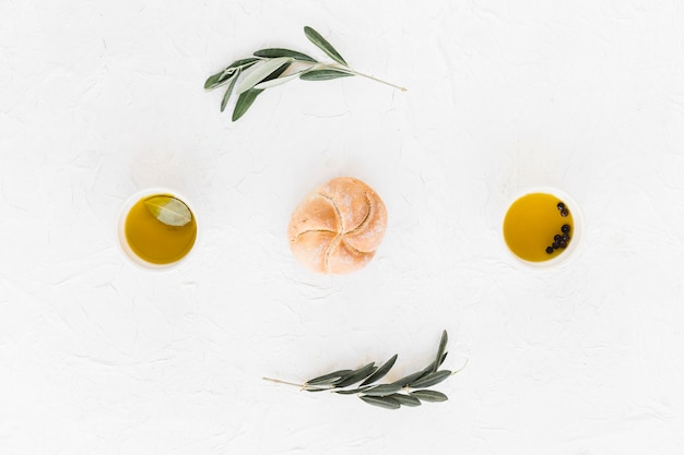 Free photo bun between the black pepper and olive oil bowls on white background