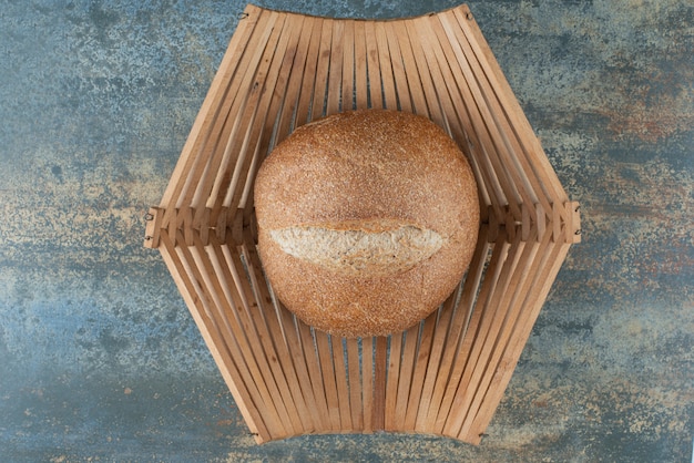 Free photo a bun of fresh brown bread on wooden basket