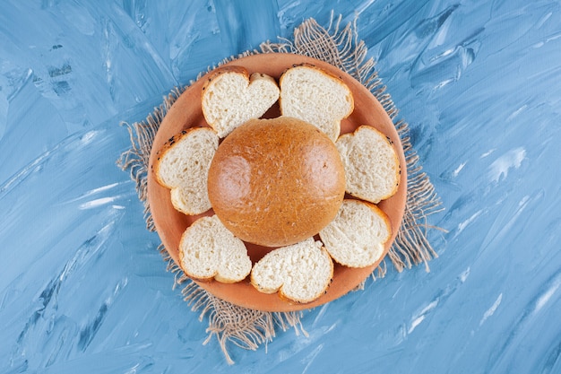 Bun and sliced bread on plate on burlap napkin on blue. 