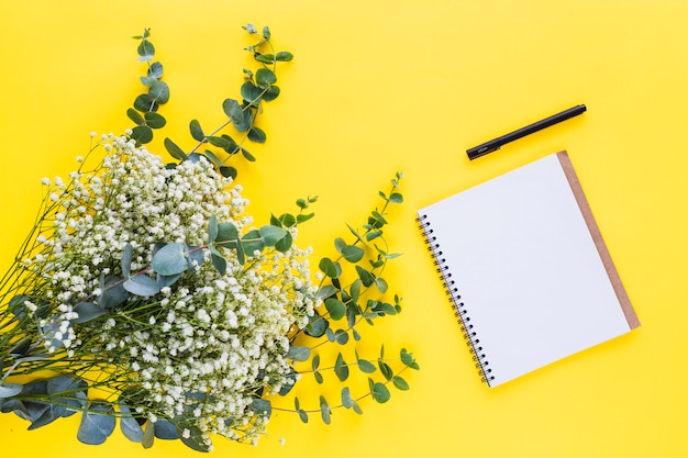 Bunch of baby's-breath flowers and spiral notepad with pen on yellow backdrop