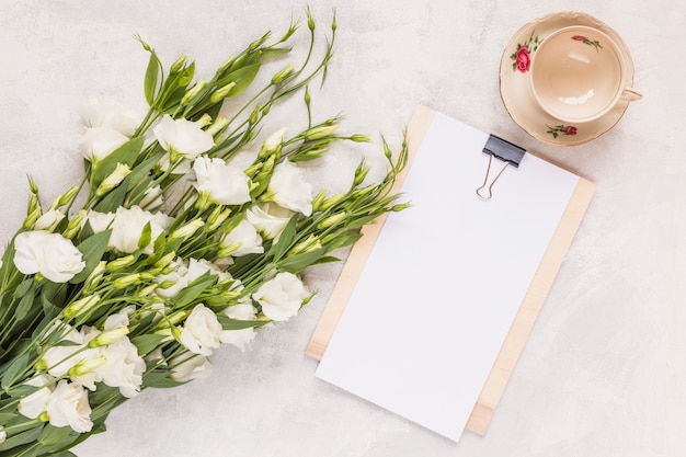 Bunch of beautiful eustoma flowers with clipboard and ceramics empty cup on white background