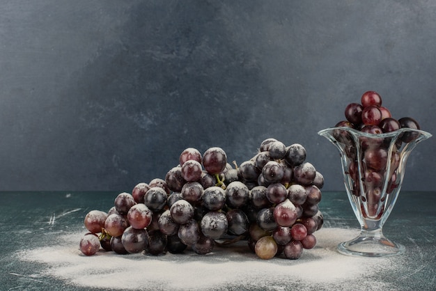 Free photo bunch of black grapes in glass and on marble table.