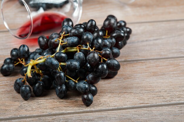 A bunch of black grapes and a glass of wine on wooden surface