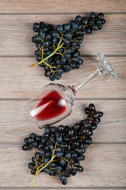 A bunch of black grapes and a glass of wine on wooden table