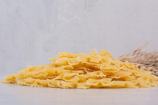 Bunch of farfalle pasta on white table with wheat.