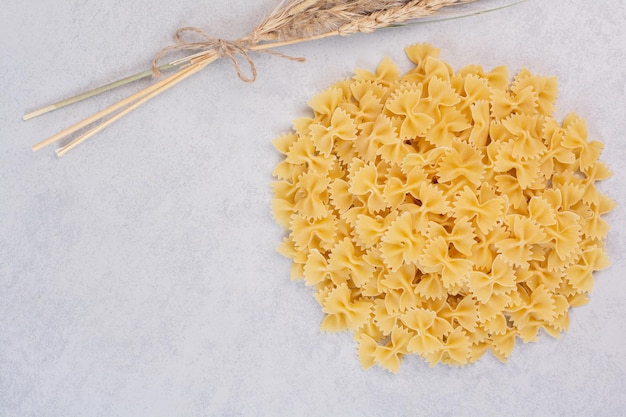 Bunch of farfalle pasta on white table with wheat.