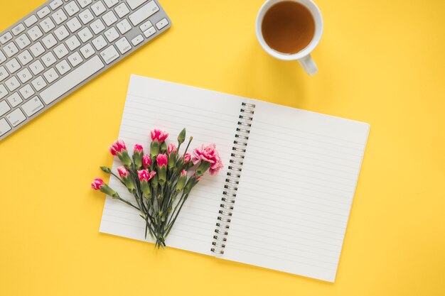 Bunch of flowers on notebook near cup of drink and keyboard
