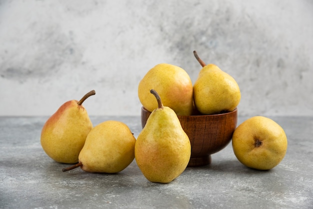 Bunch of fresh bio pears in wooden bowl on marble surface. 