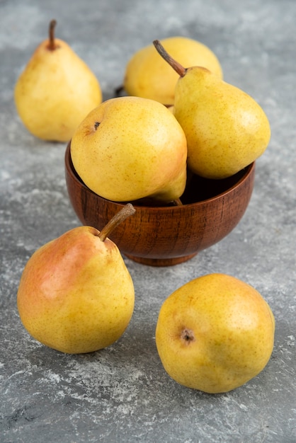 Bunch of fresh bio pears in wooden bowl on marble surface. 