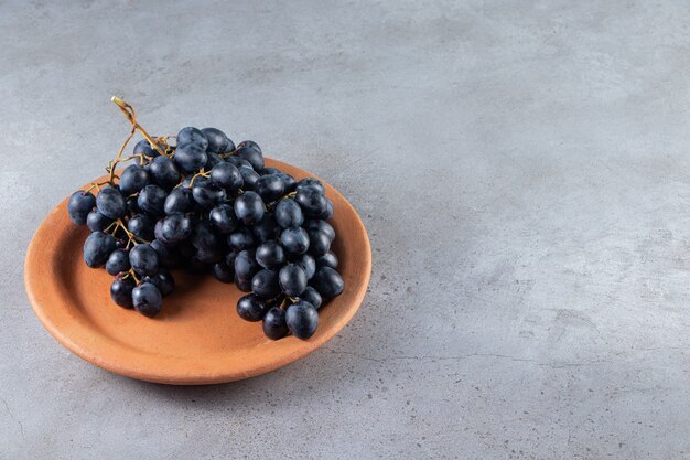 Bunch of fresh black grape in clay plate on stone table. 