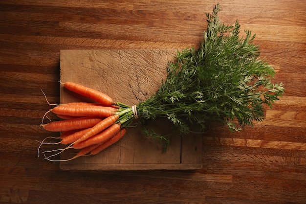 Free photo a bunch of fresh carrots on a weathered old cutting board with deep cuts on a beautiful wooden brown table, top view