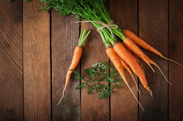 Bunch of fresh carrots with green leaves over wooden table