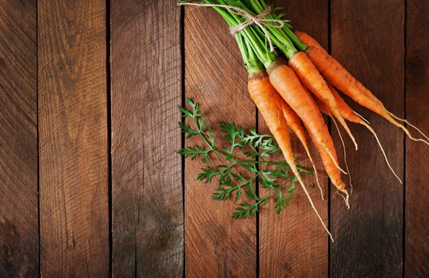 Bunch of fresh carrots with green leaves over wooden table