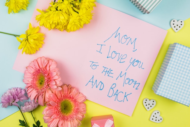 Bunch of fresh flowers near paper with words, ornamental hearts and present box