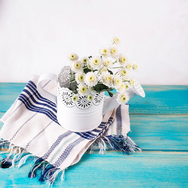 Bunch of fresh flowers in ornamental watering can on towel 