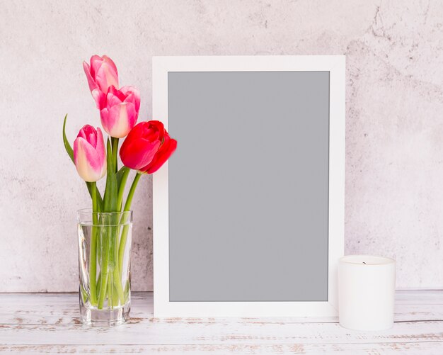Bunch of fresh flowers on stems in vase near frame and candle