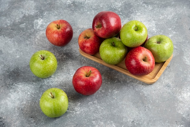 Bunch of fresh green and red apples placed on wooden plate.