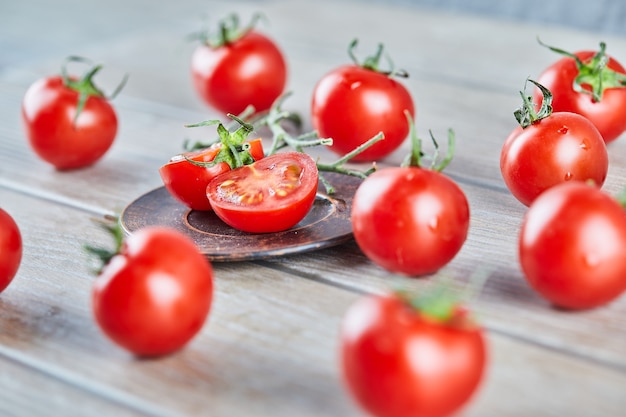 Bunch of fresh juicy tomatoes and slices of tomato on wooden table.