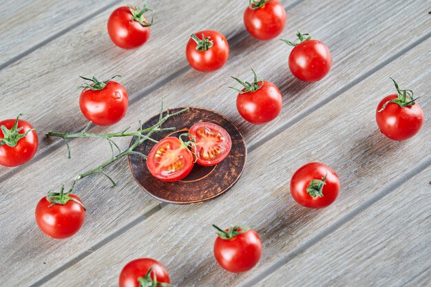 Bunch of fresh juicy tomatoes and slices of tomato on wooden table.
