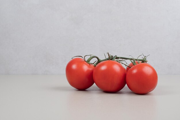 Bunch of fresh, red tomatoes with green stems on white table.