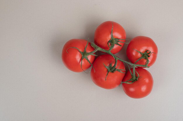 Bunch of fresh, red tomatoes with green stems on white table.