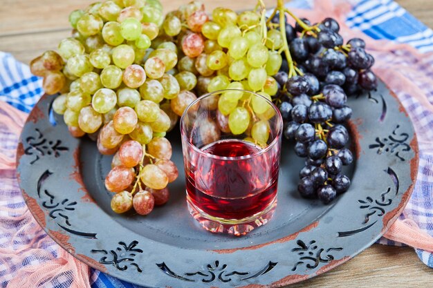 Bunch of grapes and a glass of juice on ceramic plate with tablecloths.