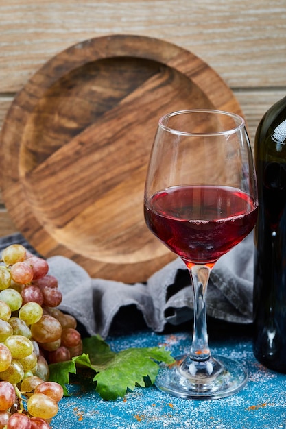 Гроздь винограда, стакан красного вона и бутылка вона на синем и деревянном.