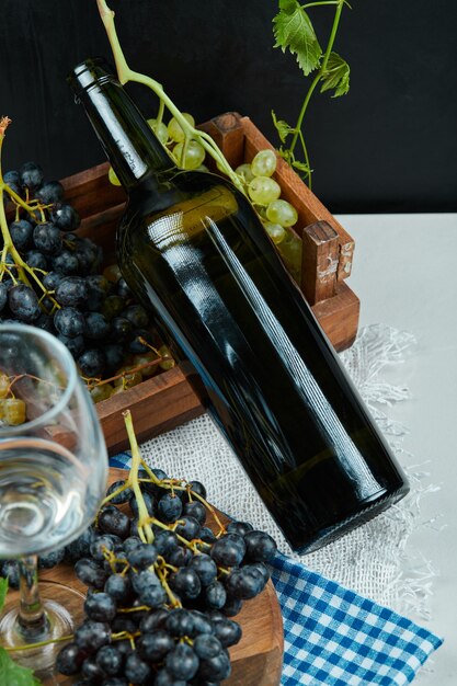 Гроздь винограда с бокалом вина и бутылкой на белом столе. Фото высокого качества