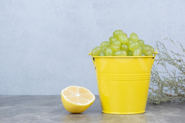 ハーフカットレモンとバケツの緑のブドウの束。