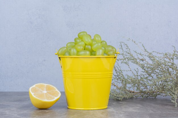 Гроздь зеленого винограда в ведре с разрезанным наполовину лимоном.