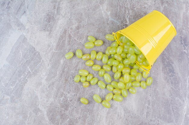 Bunch of green grapes out of bucket on stone surface. 