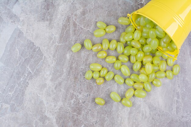 Bunch of green grapes out of bucket on stone surface. 