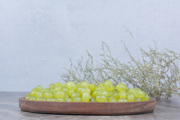 Bunch of green grapes in wooden bowl with plant. 