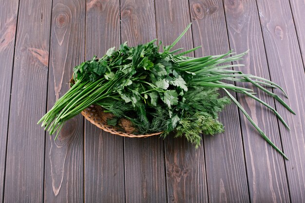 Bunch of green onion, parsley and dinn lie on little basket on dark wooden table