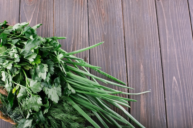Bunch of green onion, parsley and dinn lie on little basket on dark wooden table